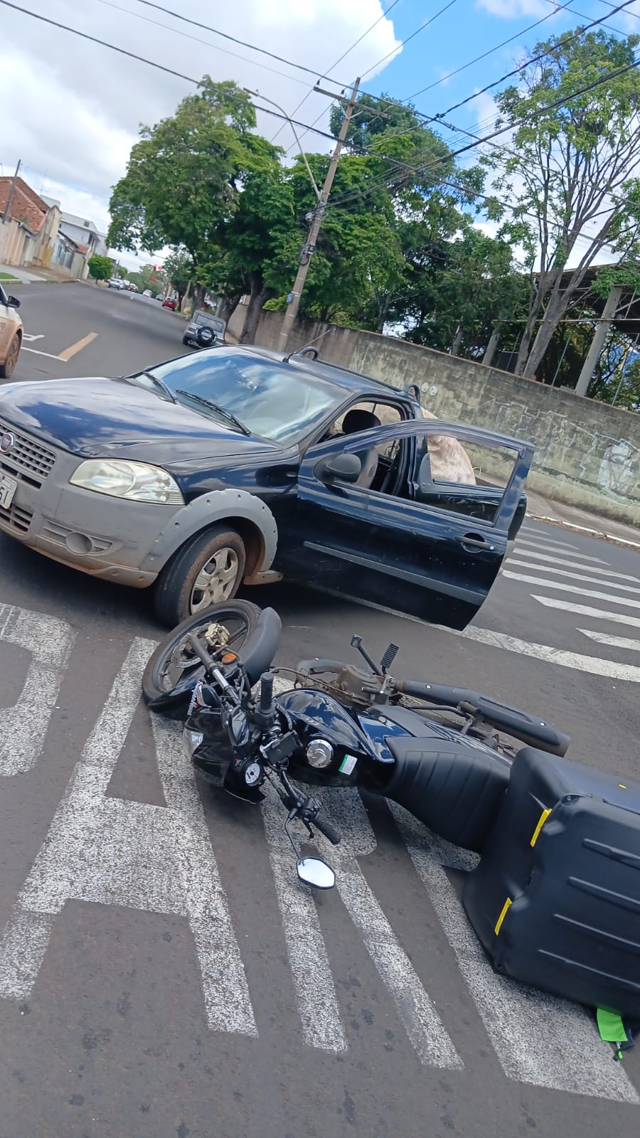 Picape Fiat Strada escura parada em cruzamento, com uma porta aberta, e uma moto caída no asfalto à frente