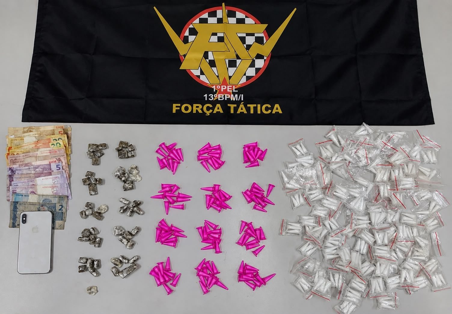 Pinos de cocaína, porções de maconha, dinheiro e celular apreendidos sobre superfície durante ação policial no Cecap.