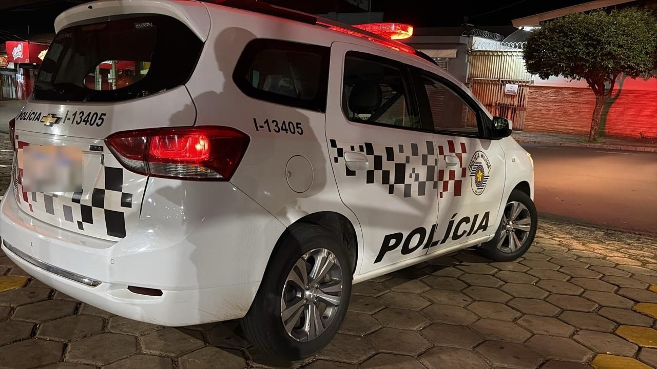 Traseira de uma viatura da Polícia Militar com as luzes acesas à noite