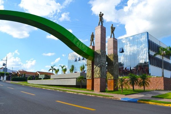 Fachada da Prefeitura de Ibaté, prédio branco de dois andares com entrada envidraçada e bandeira do município na frente.