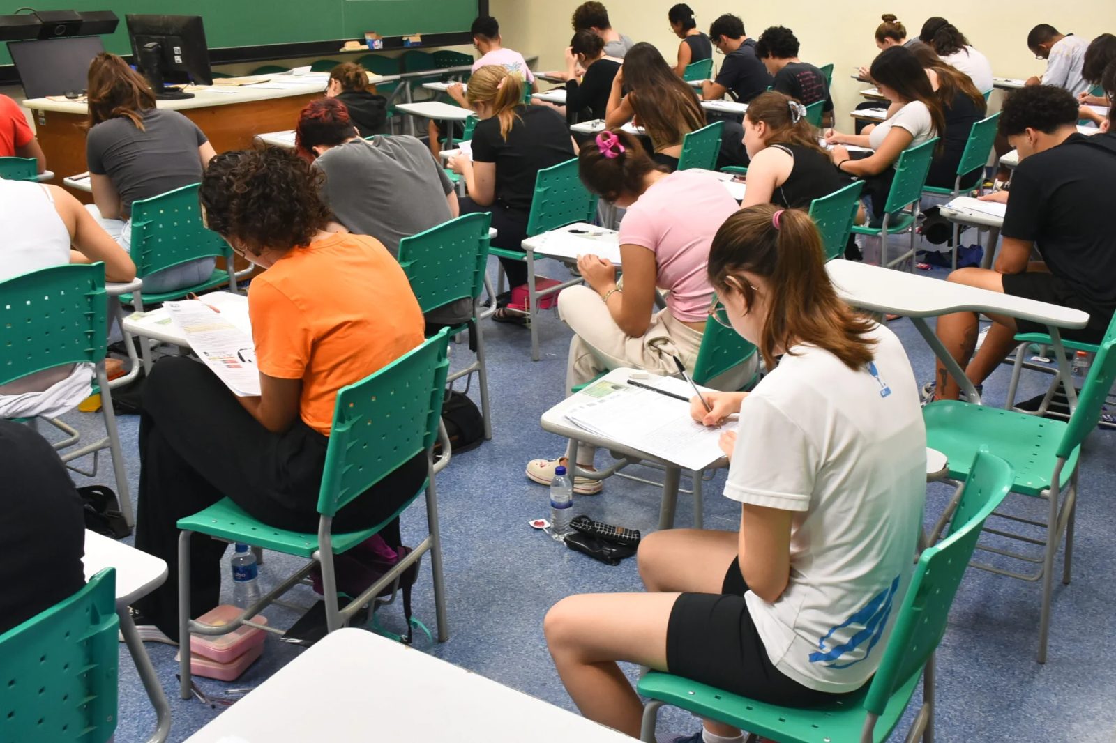 Candidatos em sala de aula durante aplicação de prova de vestibular, com carteiras organizadas em fileiras.