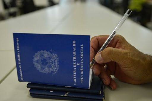 Mão assina carteira de trabalho em imagem ilustrativa